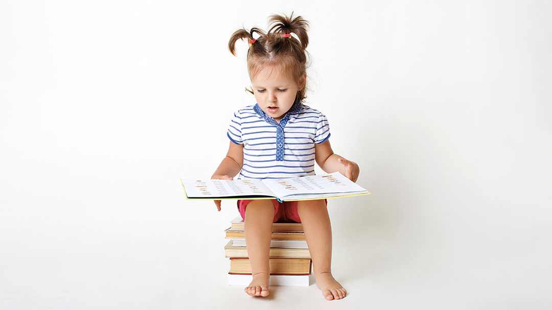 little girl reading a book sitting on a pile of books