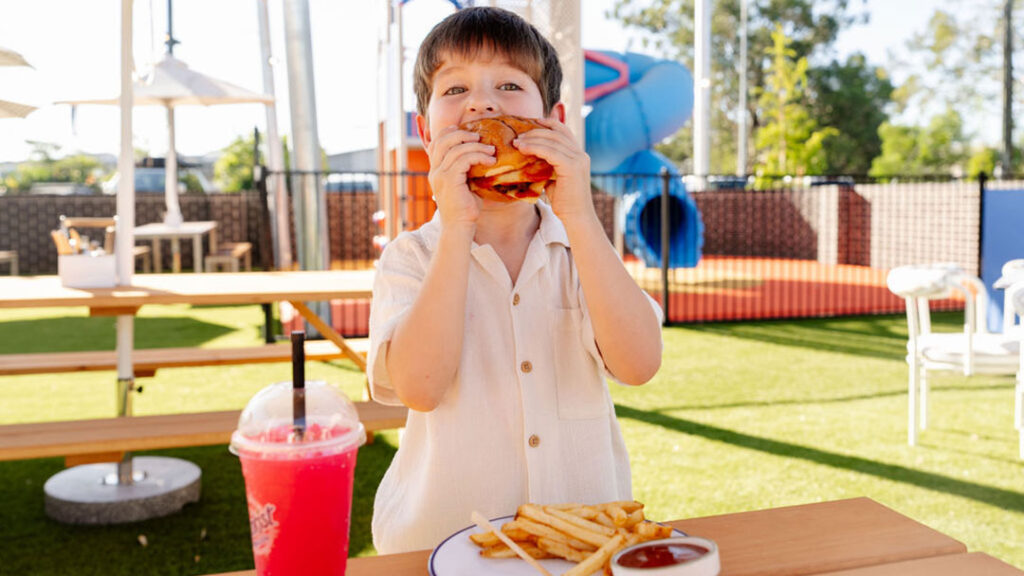 Sands-tavern2026_burger | Kids in Brisbane, Gold Coast, Sunshine Coast | Kotc Boy Enjoying a Burger at the Sands Tavern