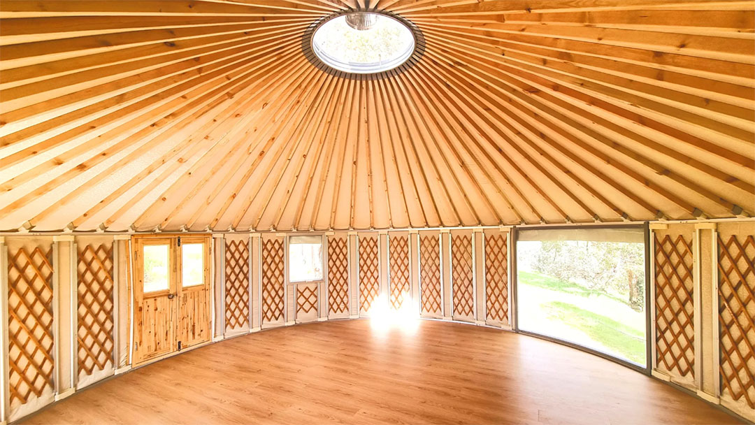Yurt2 | Kids in Brisbane, Gold Coast, Sunshine Coast | Kotc Circular Wooden Interior of a Yurt with Lattice Walls, a Central Skylight, and Large Curved Windows Overlooking a Green Lawn.