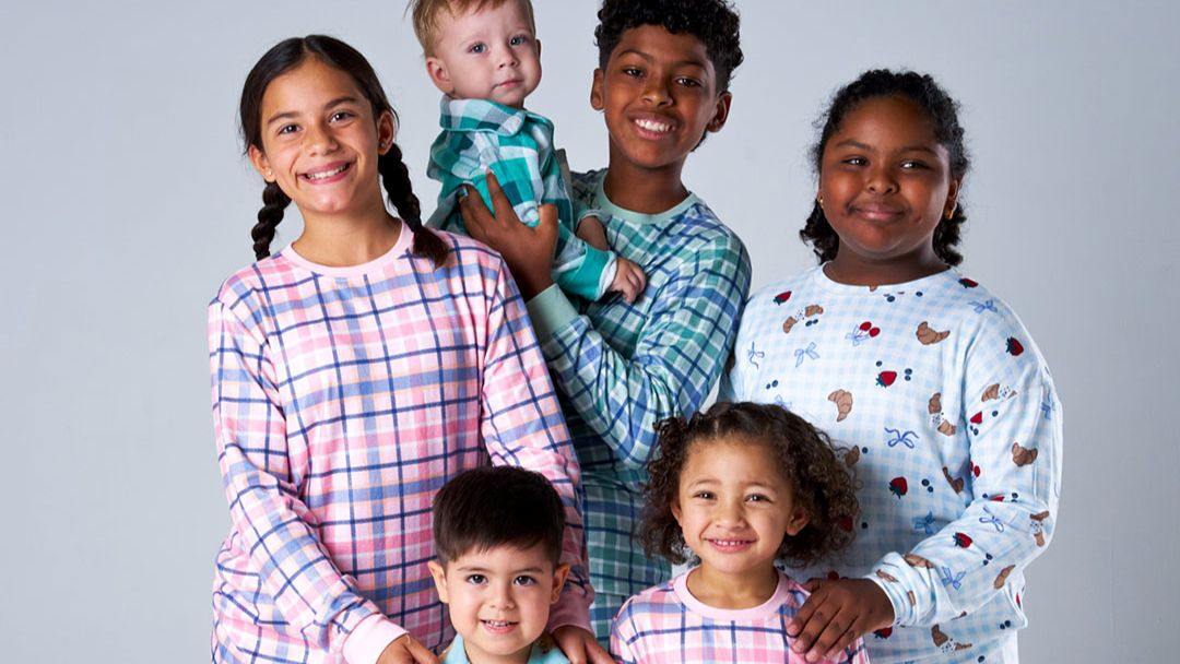 Group of six smiling children of diverse ages posing together against a light gray backdrop.