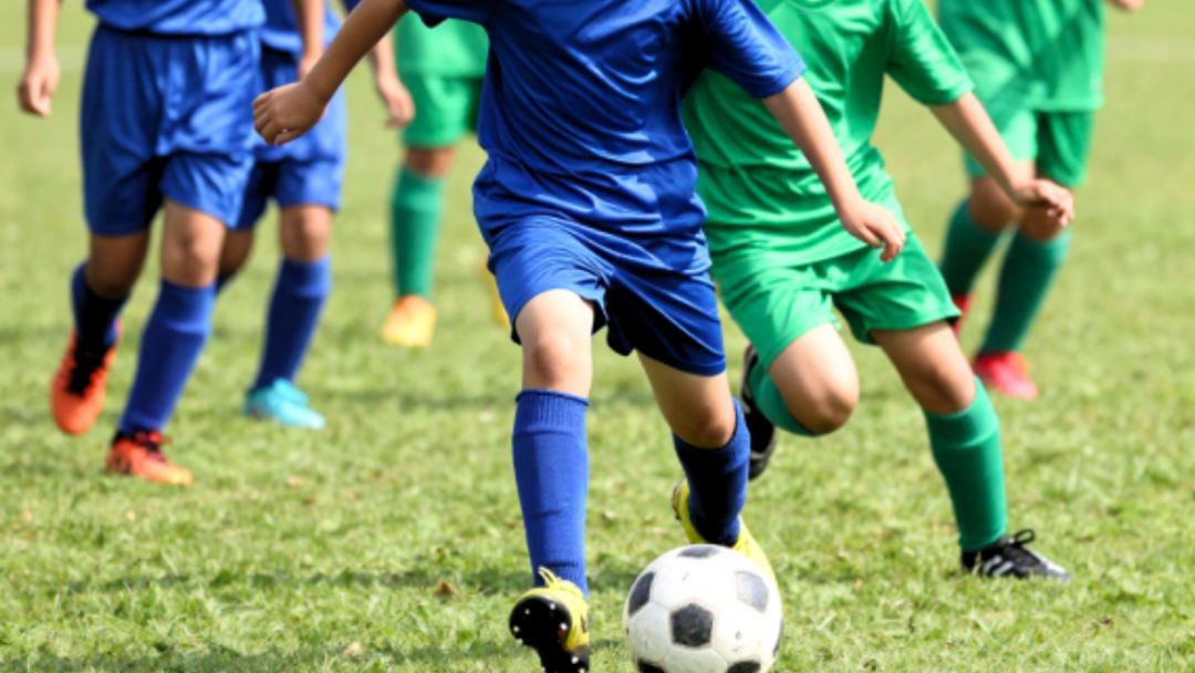 Youth Soccer Players in Blue and Green Uniforms Chase a Black-and-white Ball on a Grassy Field, Mid-game Action.