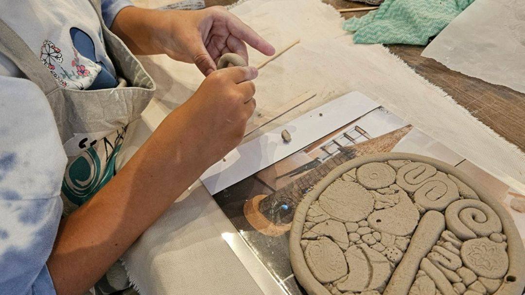Child or person shaping clay on a round clay disk with carved pieces and tools on a table, engaging in pottery art.