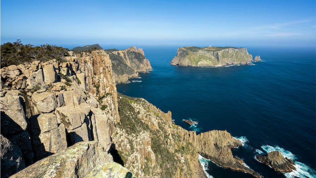 Cliffside Rocks Along a Rugged Coastline with the Deep Blue Sea Below and a Distant Green Island on the Horizon in Tasmania.
