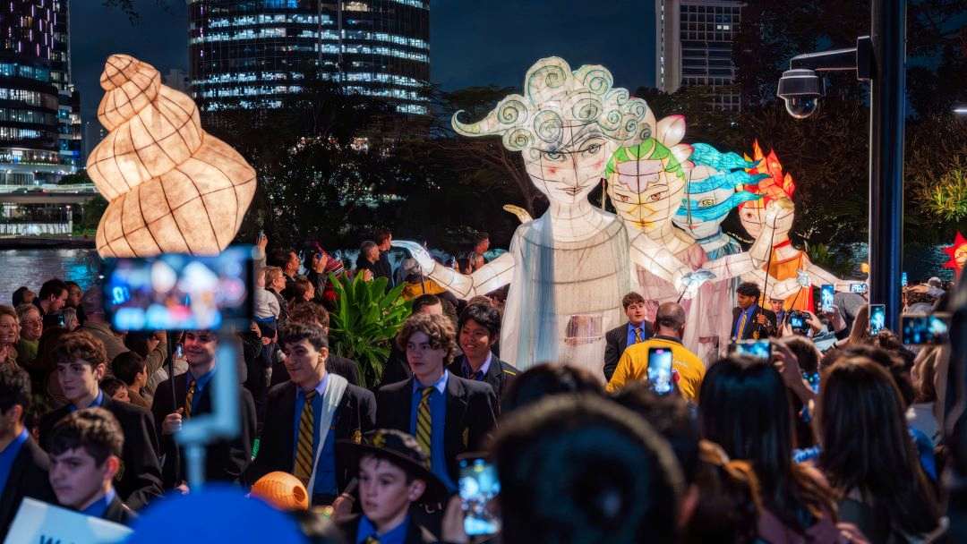 Crowded Night Festival Around Oversized Illuminated Parade Figures As People Film with Smartphones.