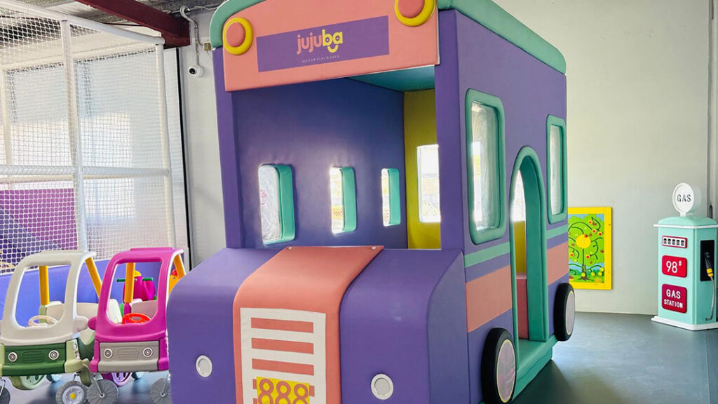 Jujuba-indoor-play-space-bus | Kids in Brisbane, Gold Coast, Sunshine Coast | Kotc Colorful Indoor Play Bus with Purple Sides, Pink Ramp, Teal Roof; Small Toy Cars Nearby.