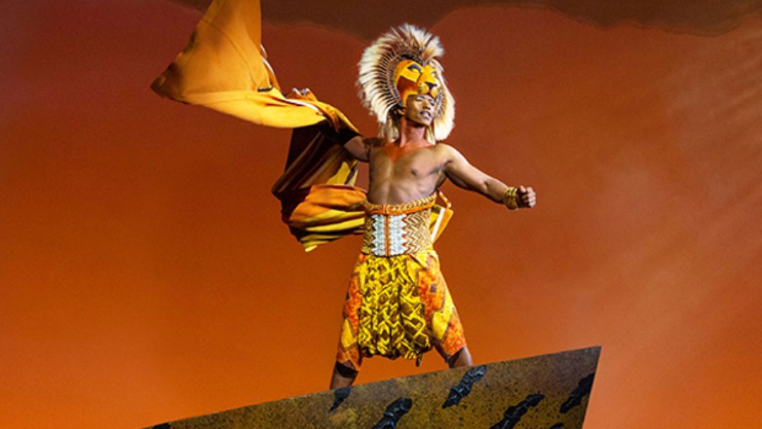 Male Carnival Performer in a Bright Yellow‑orange Costume with a Feather Headdress, Striking a Dynamic Pose on Stage