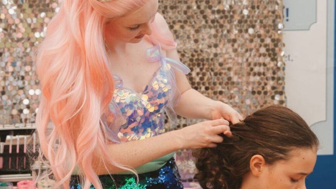 0921_royalmailhotel_marine_hero | Kids in Brisbane, Gold Coast, Sunshine Coast | Kotc Stylist with Pink Hair Styles a Client's Brown Hair During a Salon Session with a Sparkly Backdrop.