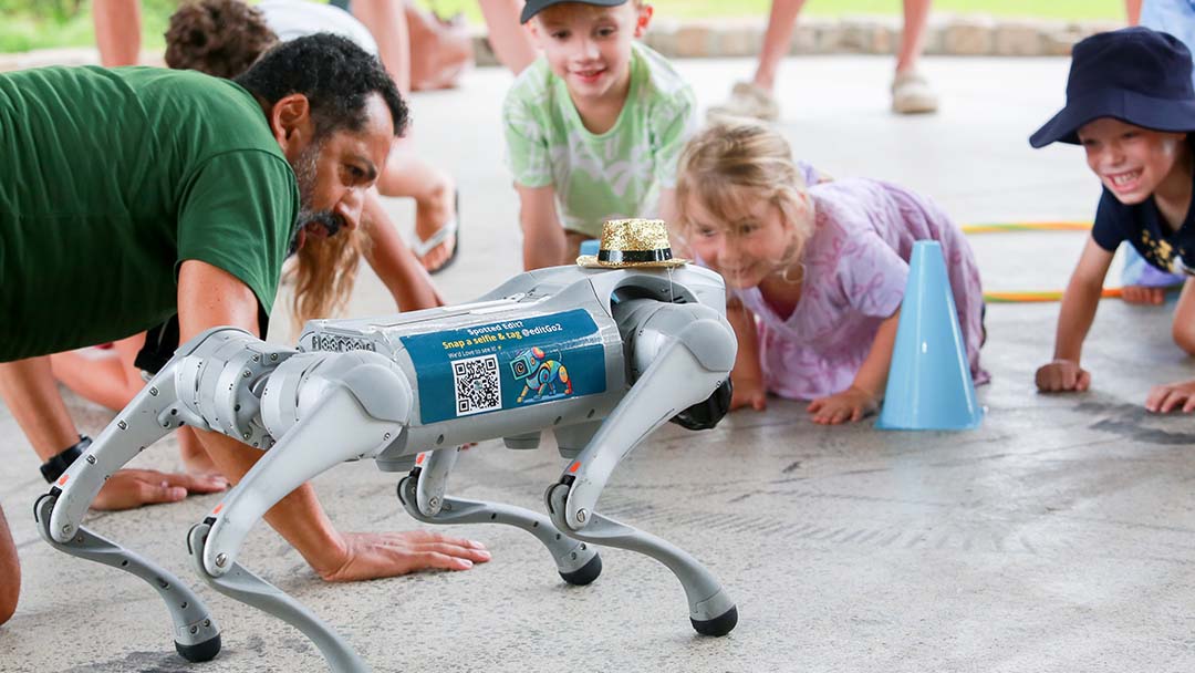 Robotic Four-legged Dog on a Gray Pavement As Children Watch a Demonstration Curiously.