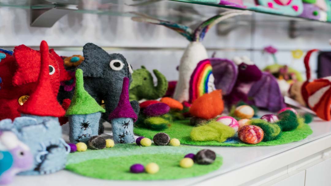 Colorful Felt Plush Toys Arranged on a Green Display Mat, Featuring Gnomes, a Rainbow, and Other Whimsical Creatures in a Shop Setting to Attract Customers