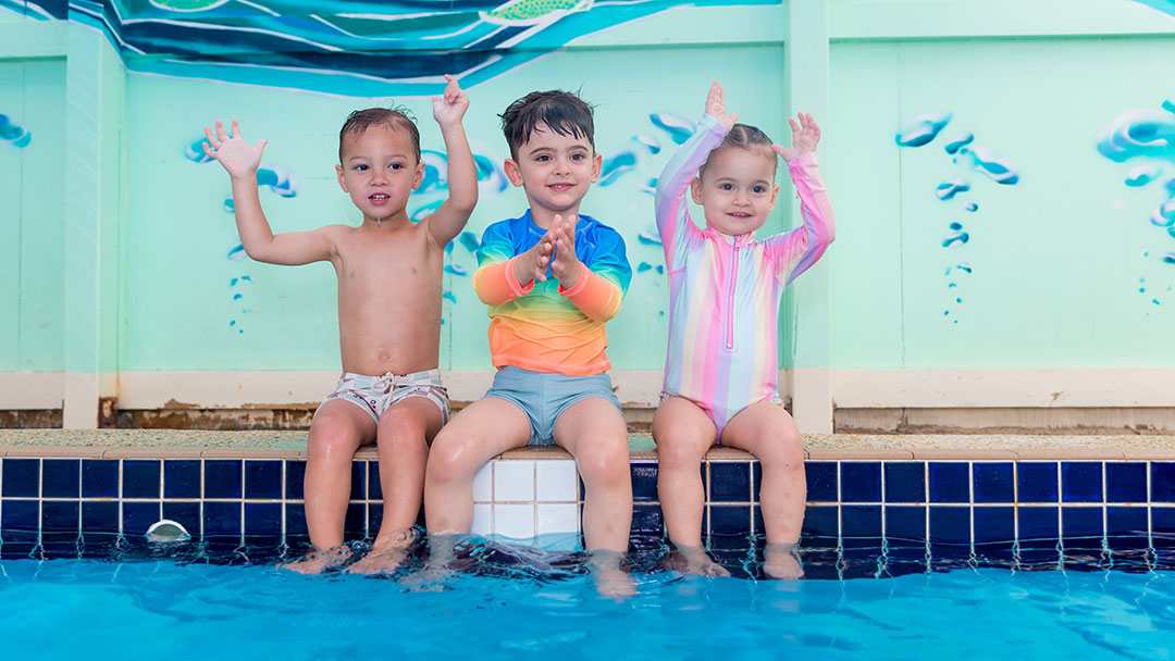 Shaplands Swim School-2 | Kids in Brisbane, Gold Coast, Sunshine Coast | Kotc Three Young Children Sitting on the Side of the Pool Ready for a Swim Lesson