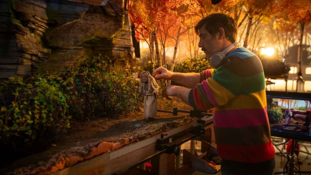Stop-motion Animator Carefully Positioning a Handmade Puppet on an Elaborate Miniature Autumn Forest Set During the Production of Wildwood.