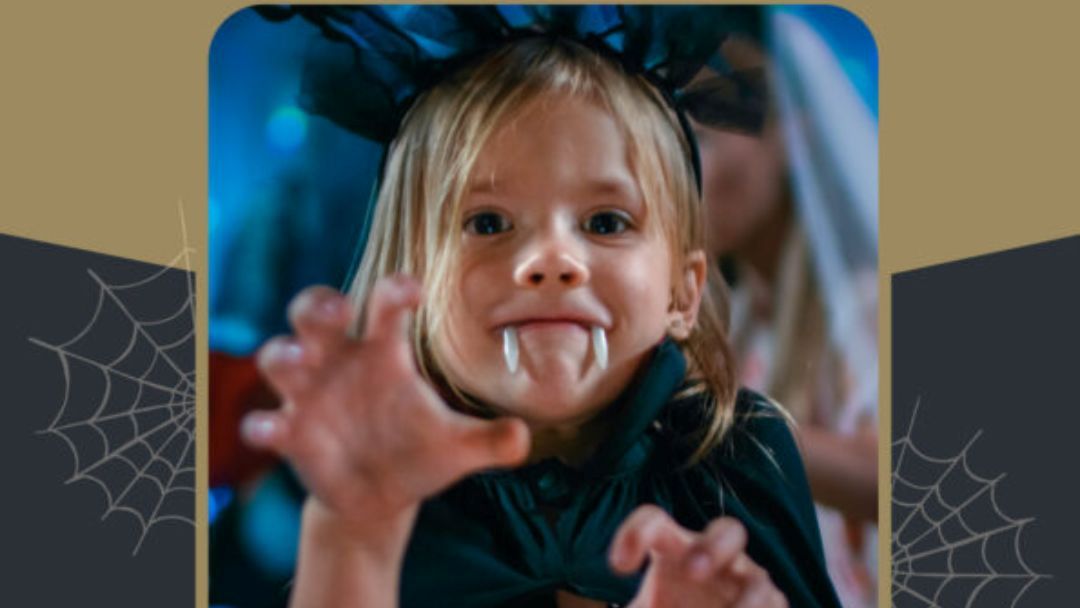 1013_koalatavern_halloween_hero | Kids in Brisbane, Gold Coast, Sunshine Coast | Kotc Young Girl in a Black Cape with Vampire Fangs Leans Toward the Camera, Hands Reaching Forward in a Playful Halloween Pose.