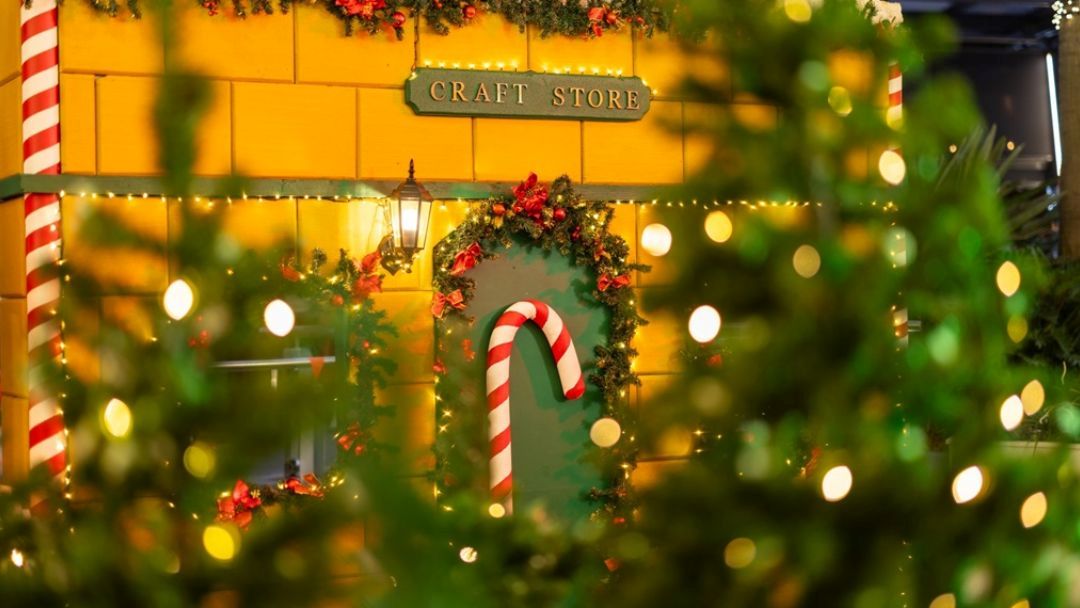 Festively Decorated Craft Store Facade with a Wreath, Candy Cane Arch, and Twinkling Lights by a Warm Yellow Wall.