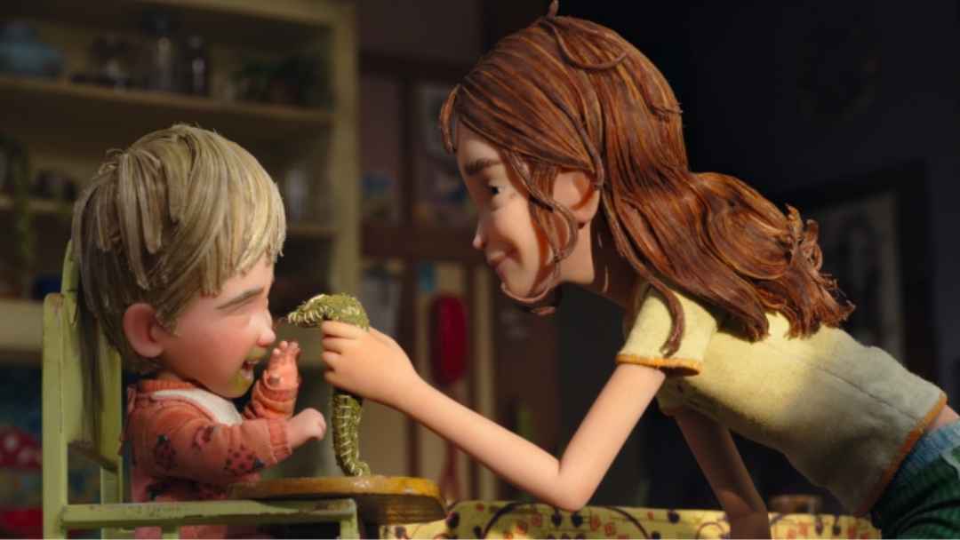 Stop-motion Animated Scene from Wildwood Showing a Young Girl Smiling at a Baby in a Highchair While Holding a Small Green Creature.